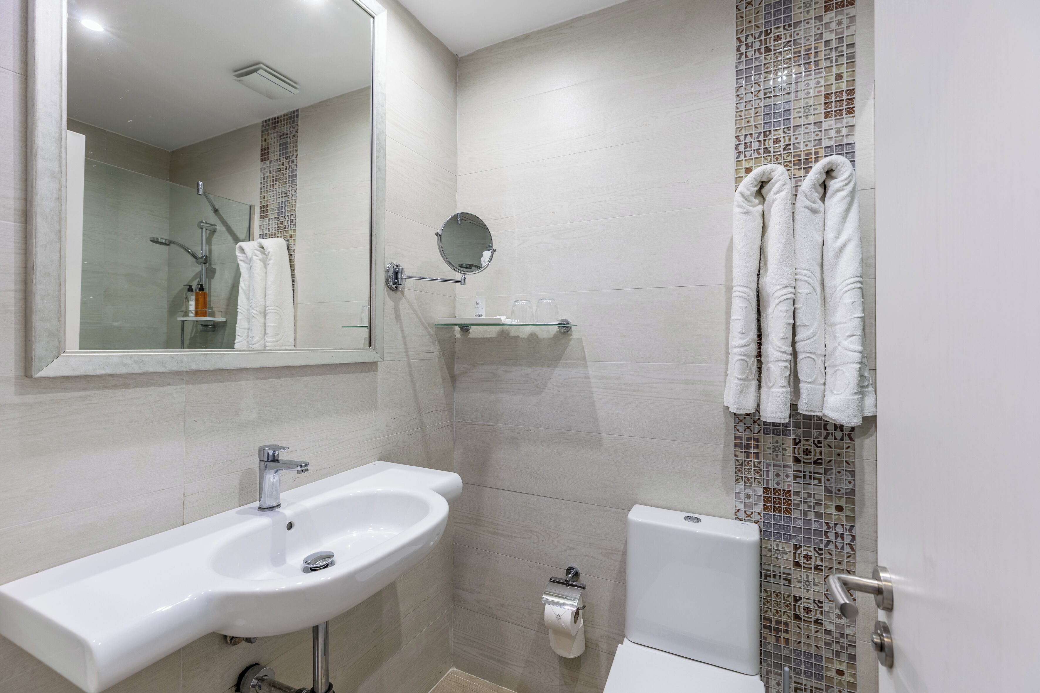 A modern bathroom with a sink, mirror, shower, and toilet.