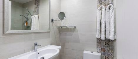 A modern bathroom with a sink, mirror, shower, and toilet.