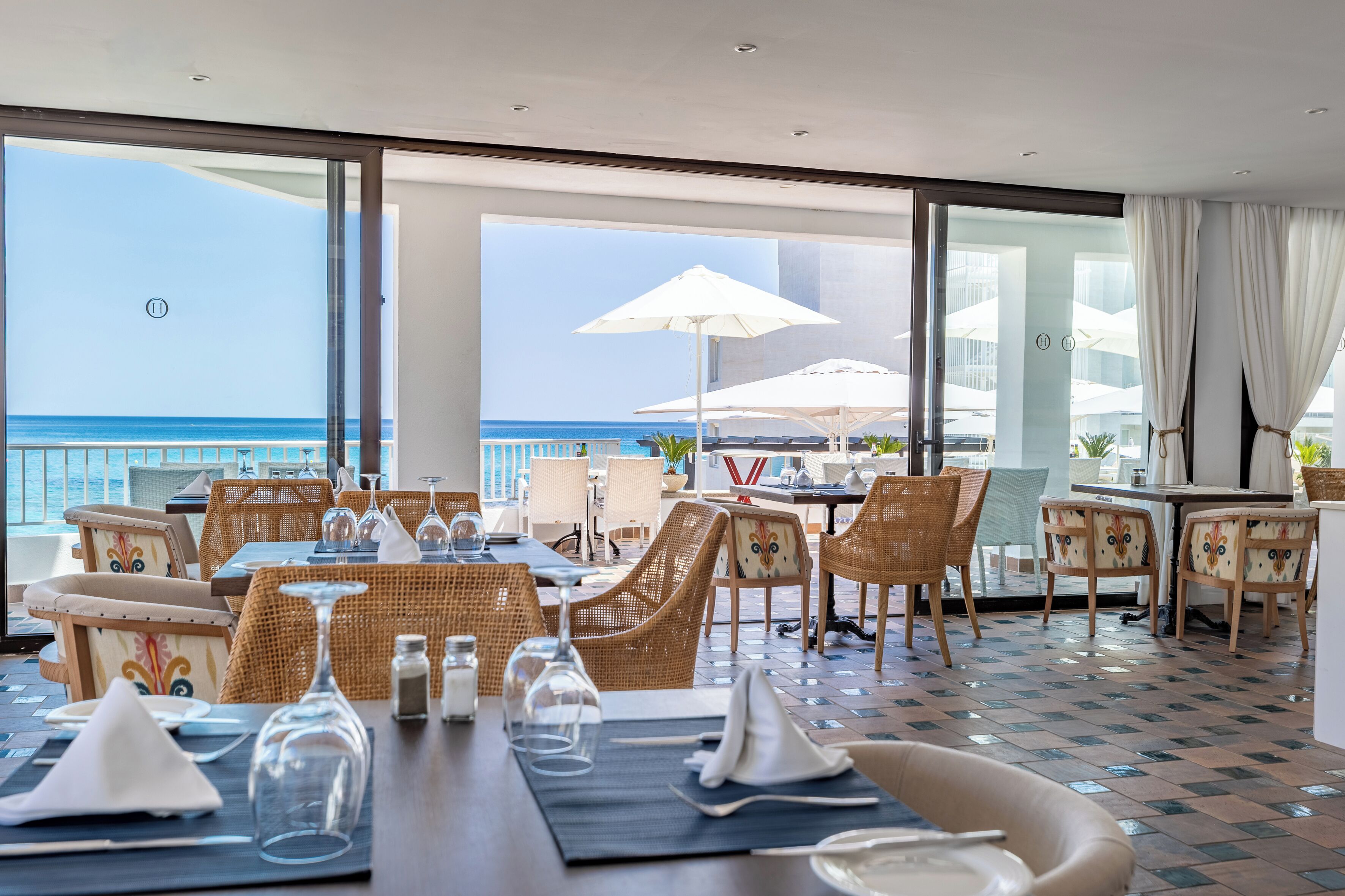 A dining area with wicker furniture, glassware, and a view of the ocean.