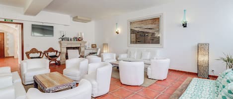 A spacious living room with white furniture, a fireplace, and a large painting on the wall.