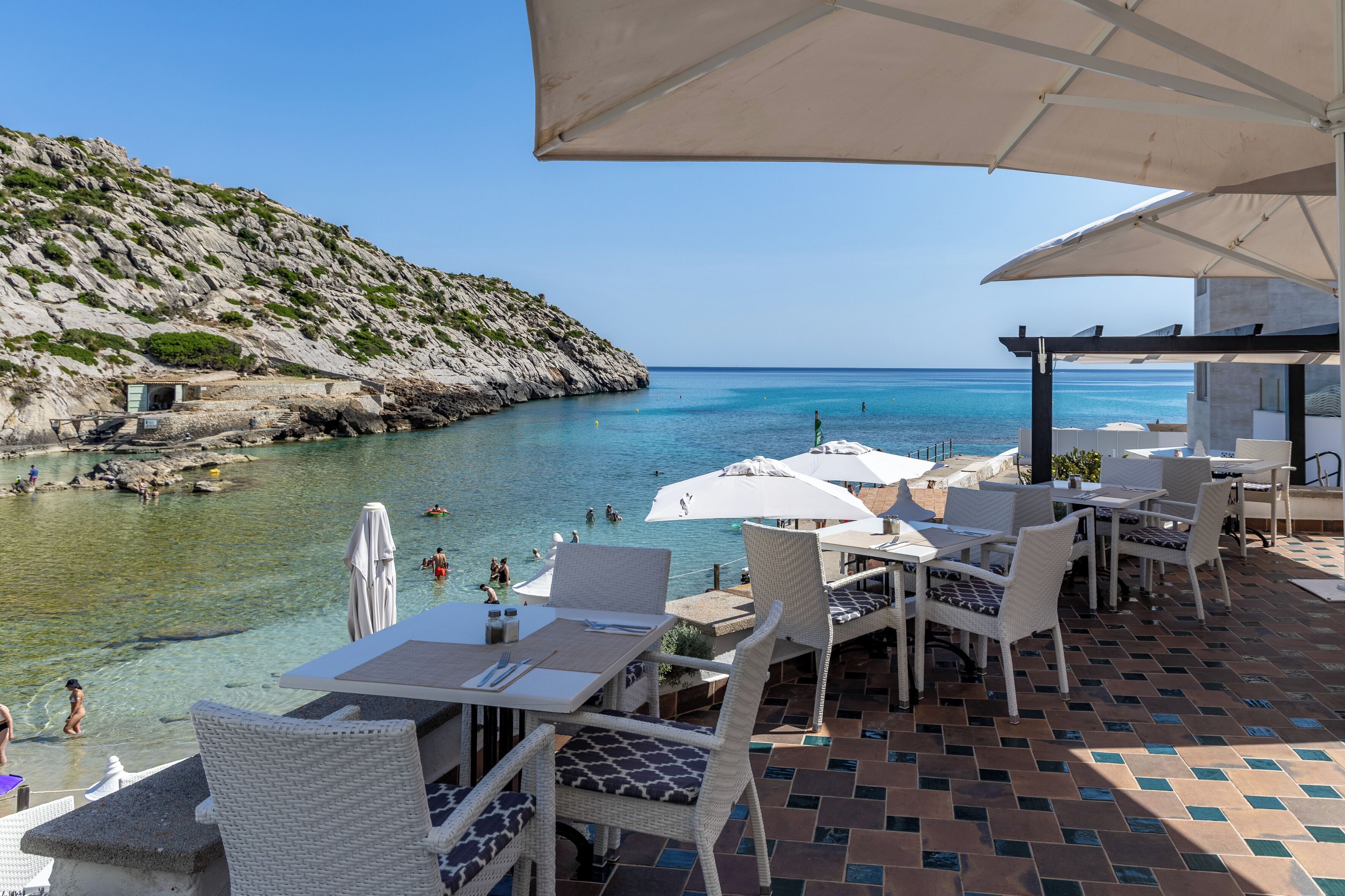 Una terraza frente al mar con asientos al aire libre, vistas al océano y una ladera rocosa.