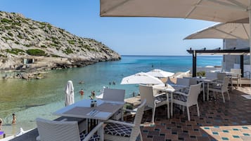 Una terraza frente al mar con asientos al aire libre, vistas al océano y una ladera rocosa.