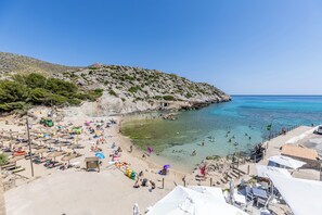 A beach with clear waters, umbrellas, and people. - Hoposa Hotel Niu (Pollenca)
