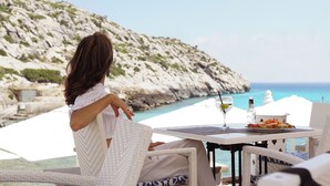Una persona sentada a una mesa con vistas al mar y acantilados rocosos.