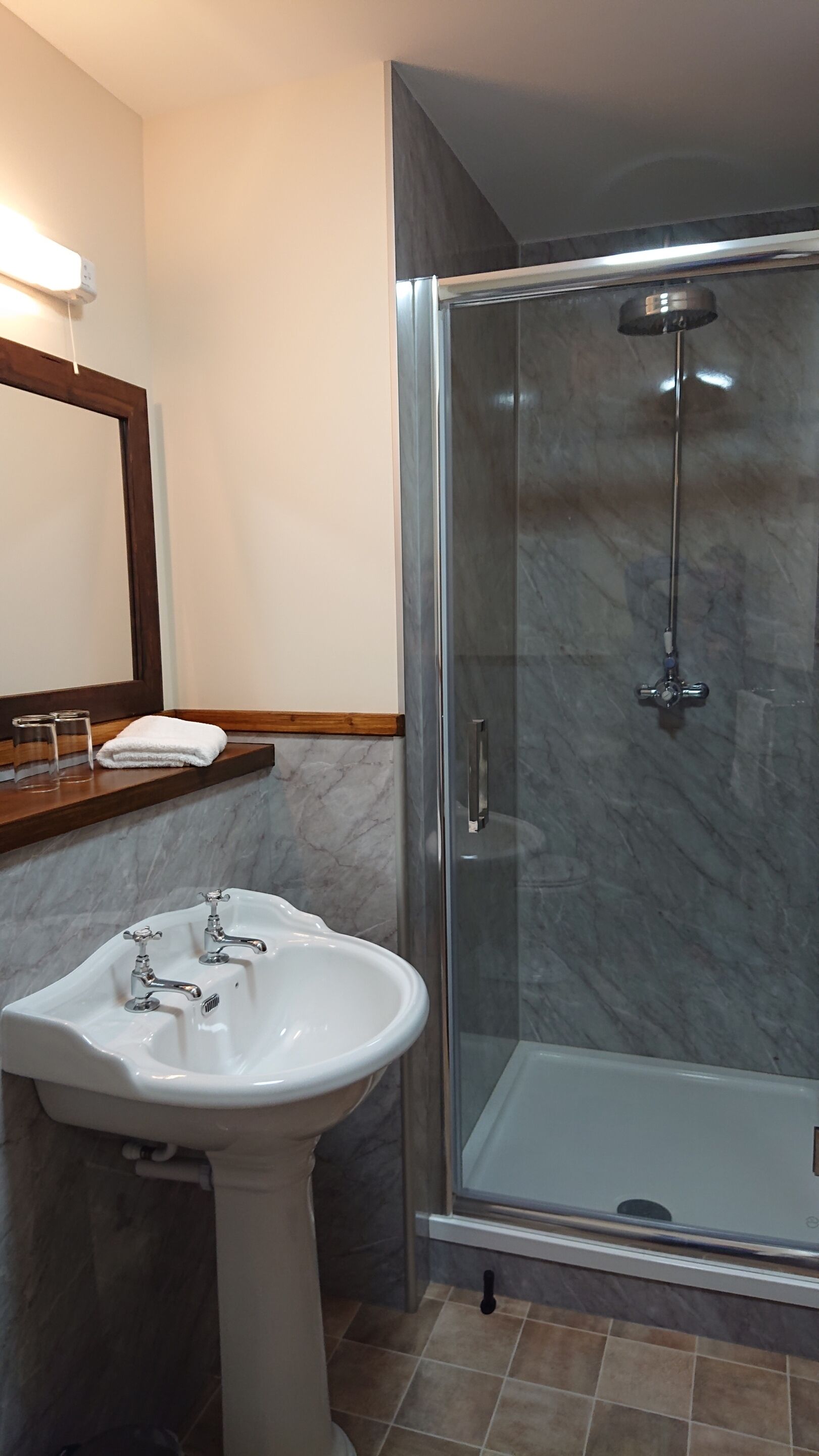 A bathroom with a pedestal sink, a glass shower enclosure, and a wooden-framed mirror.