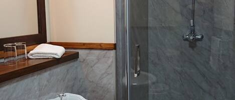 A bathroom with a pedestal sink, a glass shower enclosure, and a wooden-framed mirror.