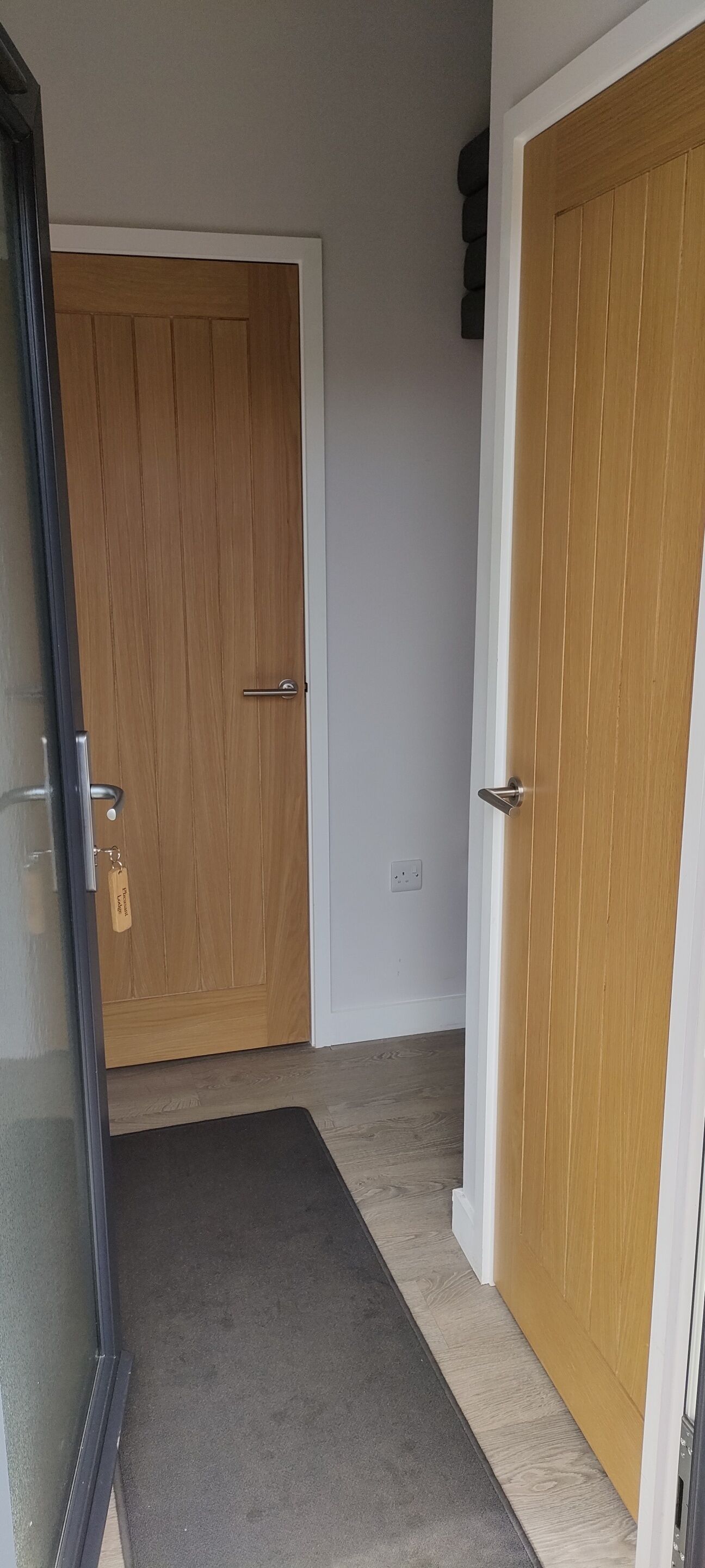 Un pasillo con dos puertas de madera, una con una mirilla y un llavero, y un suelo alfombrado.