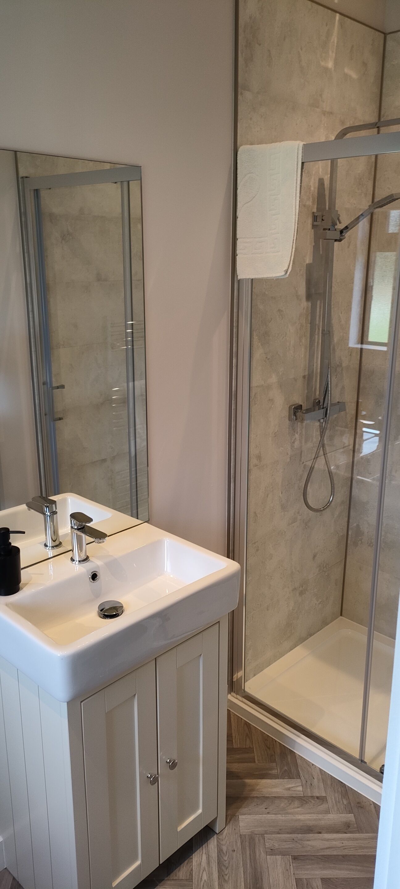 Un baño moderno con ducha de vidrio, un lavamanos blanco con dos grifos y un espejo sobre el lavamanos.
