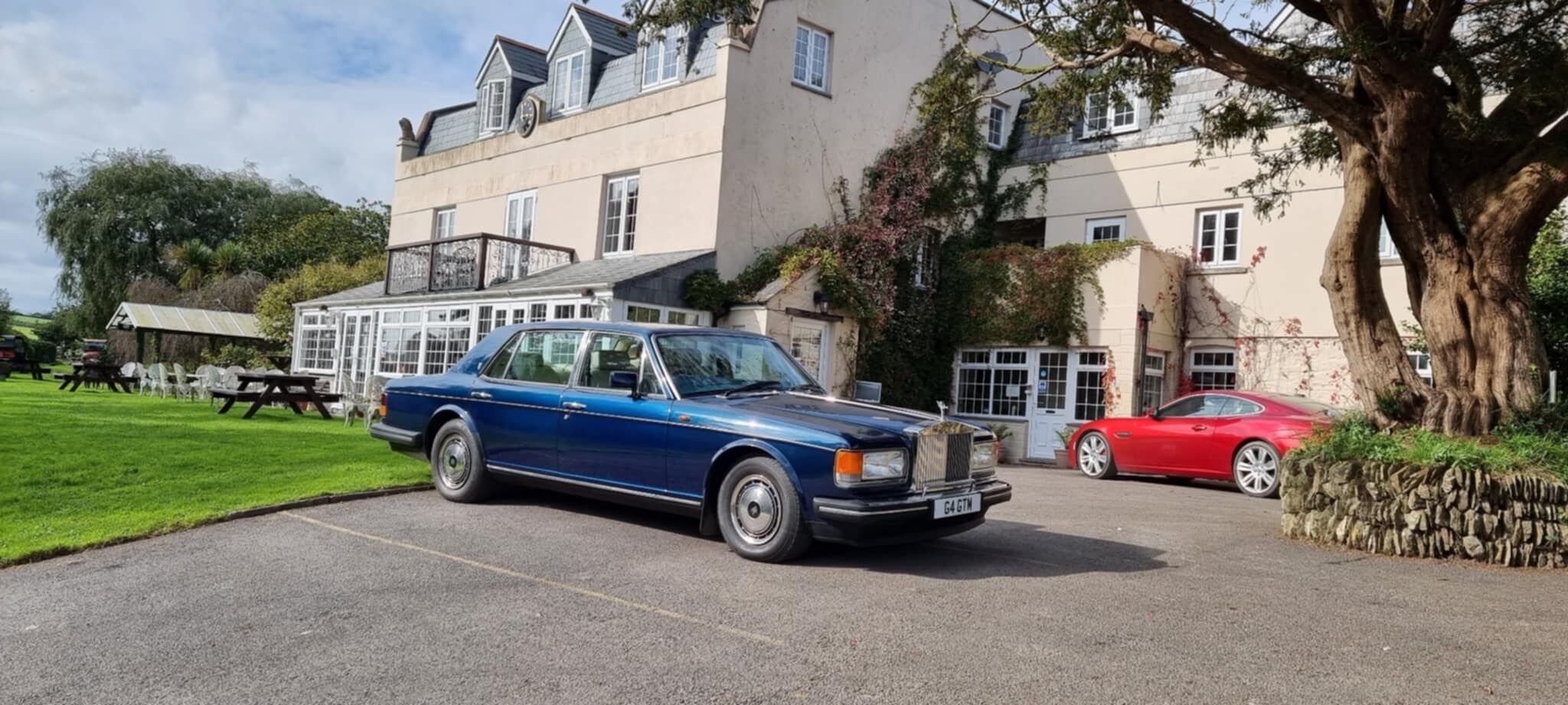 Ein blaues Auto vor einem Gebäude mit einer Steinwand, in der Nähe steht ein rotes Auto.