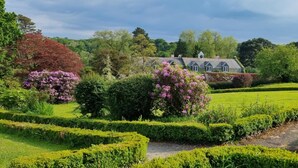 Un jardin bien entretenu, agrémenté de haies, d’arbustes en fleurs et d’une maison traditionnelle dotée d’un toit à pignon.