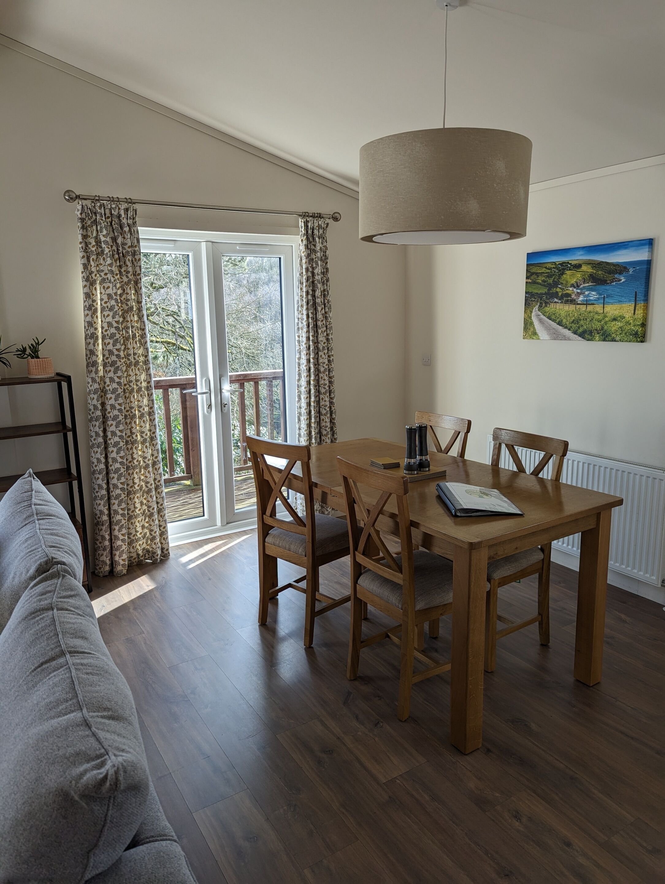 A dining area with a wooden table and chairs, a hanging lamp, and a view of the outdoors through a glass door.