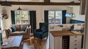 Un salon confortable avec un canapé, un fauteuil, une table basse en bois et un coin cuisine équipé d’une cuisinière et de placards.