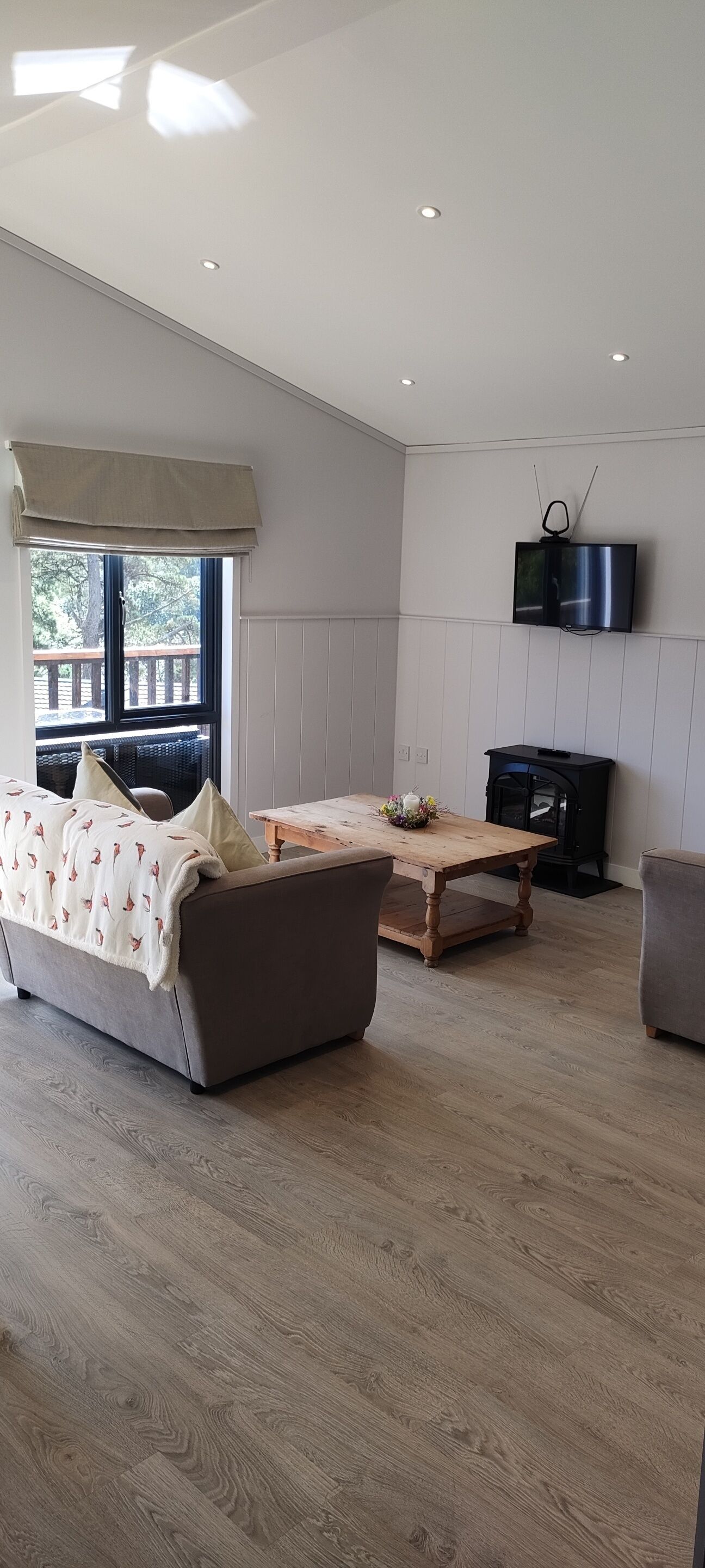 A spacious living room with a sofa, a wooden coffee table, and a television mounted on the wall.