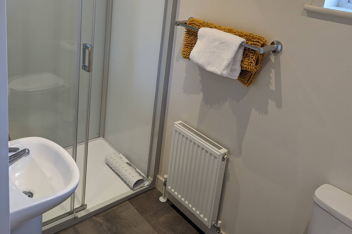 A modern bathroom with a glass-enclosed shower, a white sink, a towel rack with a yellow towel, and a radiator.