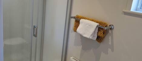 A modern bathroom with a glass-enclosed shower, a white sink, a towel rack with a yellow towel, and a radiator.