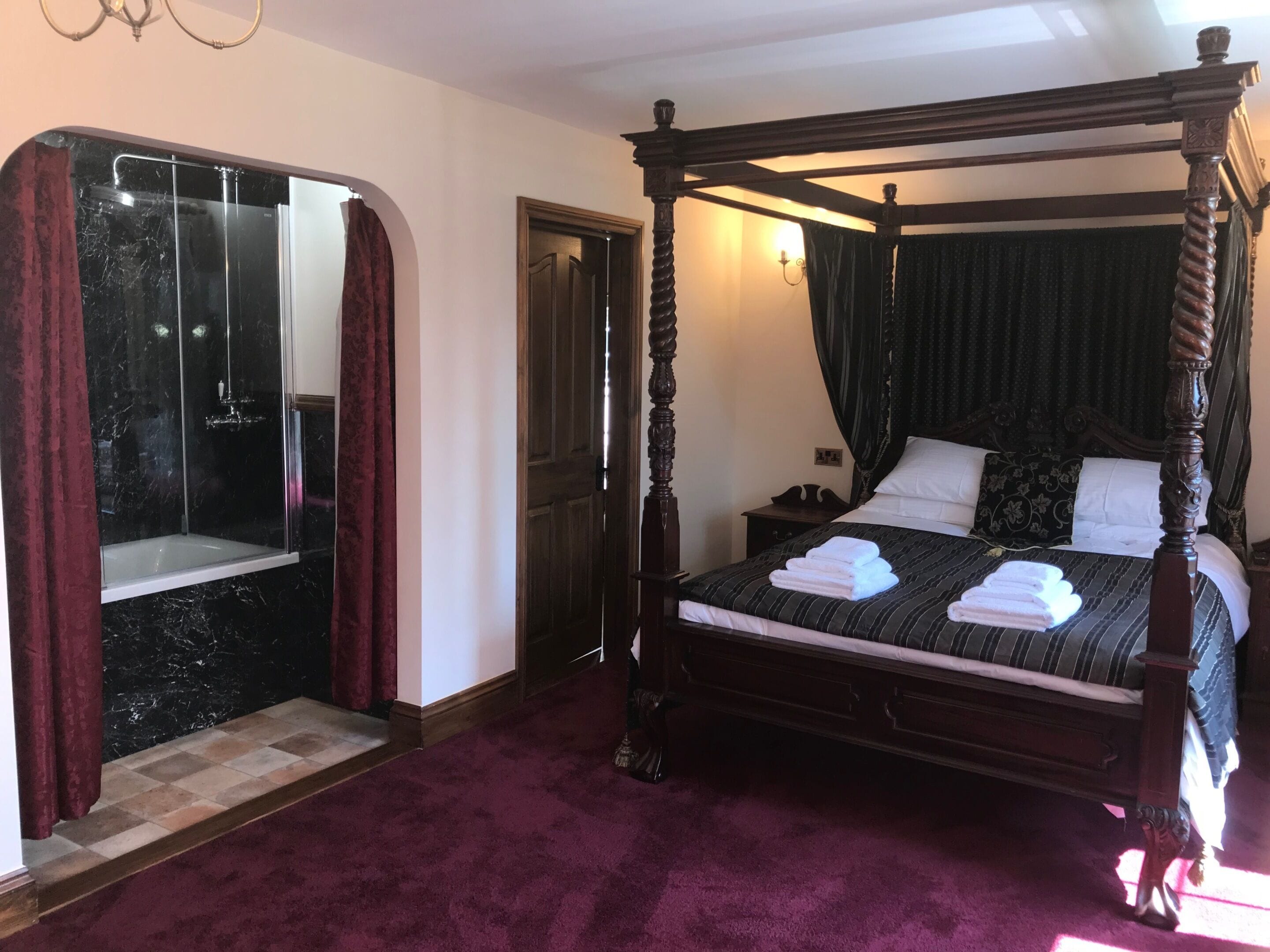 Ein Bett mit Baldachin, eine Duschkabine aus Marmor und ein rot bezogener Boden.