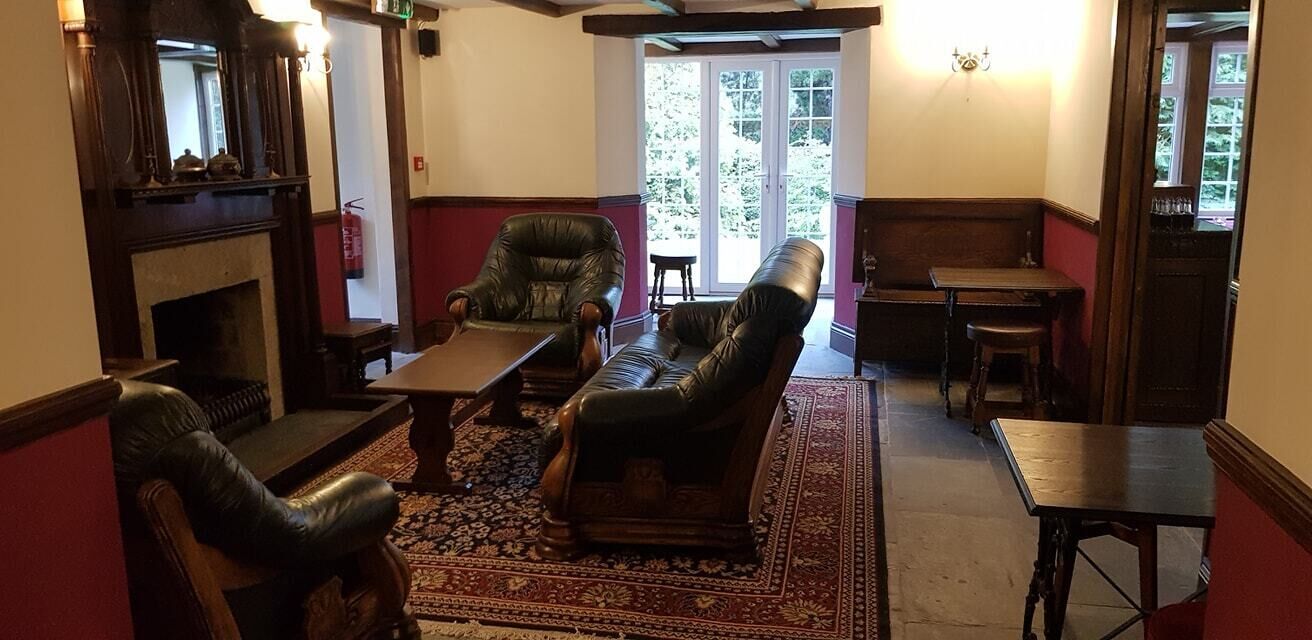 A traditional room with a fireplace, leather armchairs, a wooden table, and a patterned rug.