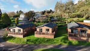 Une rangée de maisons mobiles dotées de terrasses en bois et bordées d’une pelouse, le tout entouré d’arbres et adossé à une colline où se trouvent des maisons au loin.