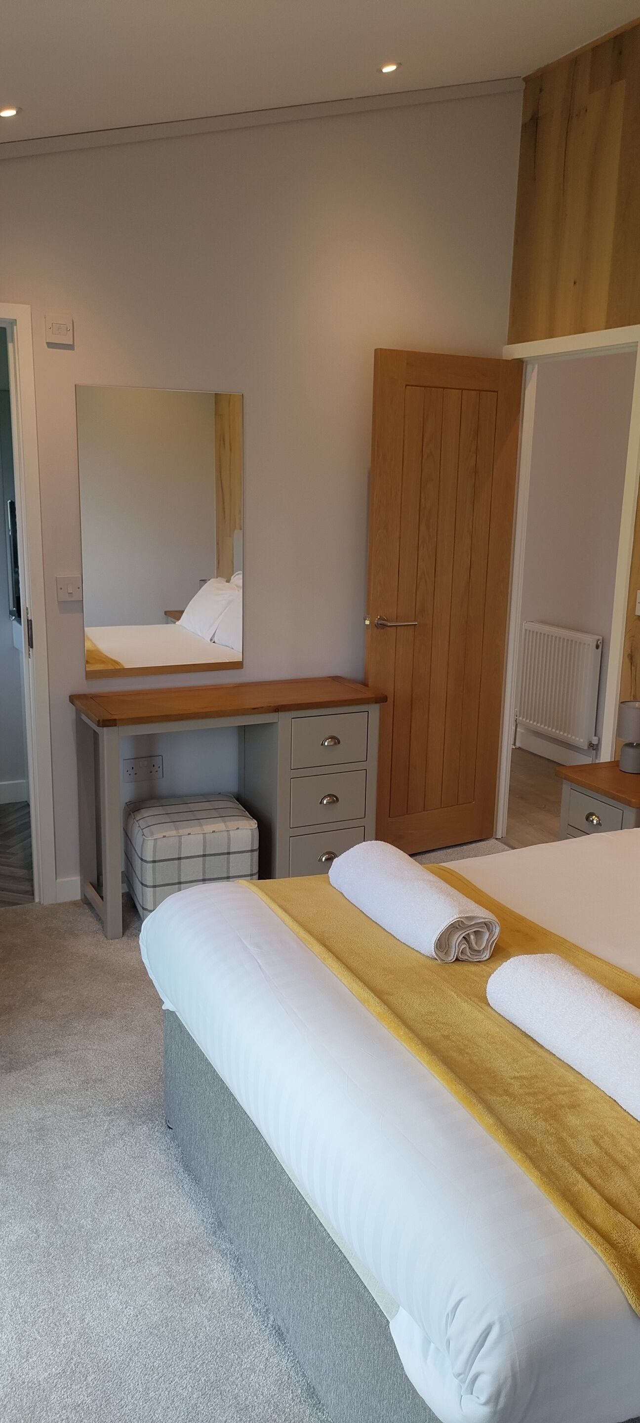 A bedroom with a bed, a desk, a chair, a mirror, and a wardrobe.