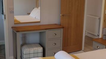 A bedroom with a bed, a desk, a chair, a mirror, and a wardrobe.