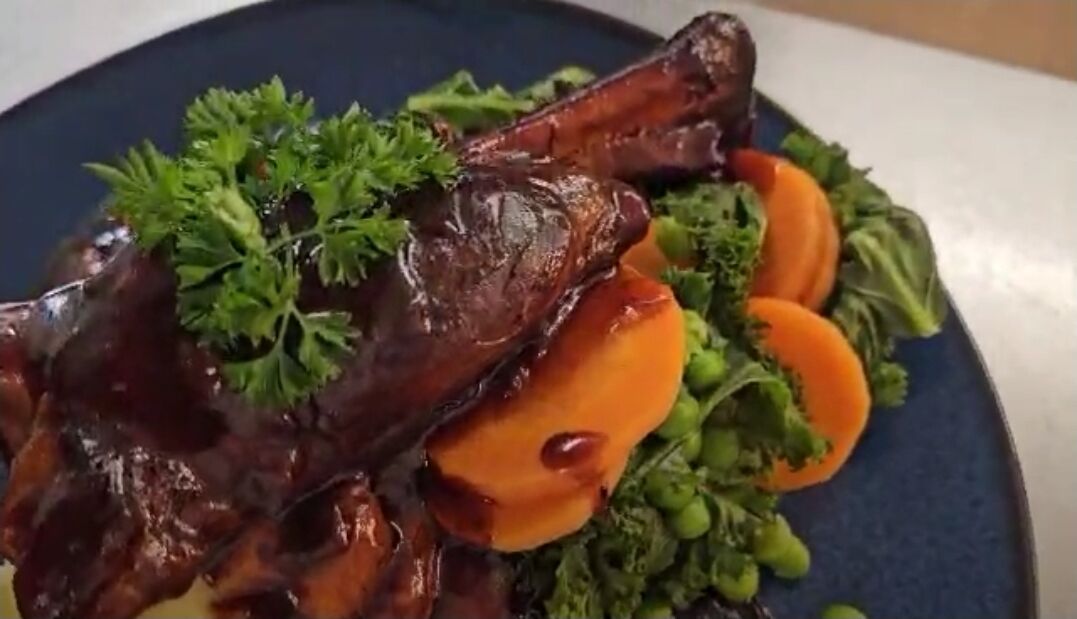 A plate with a glazed meat dish, garnished with parsley, accompanied by sliced carrots and greens.