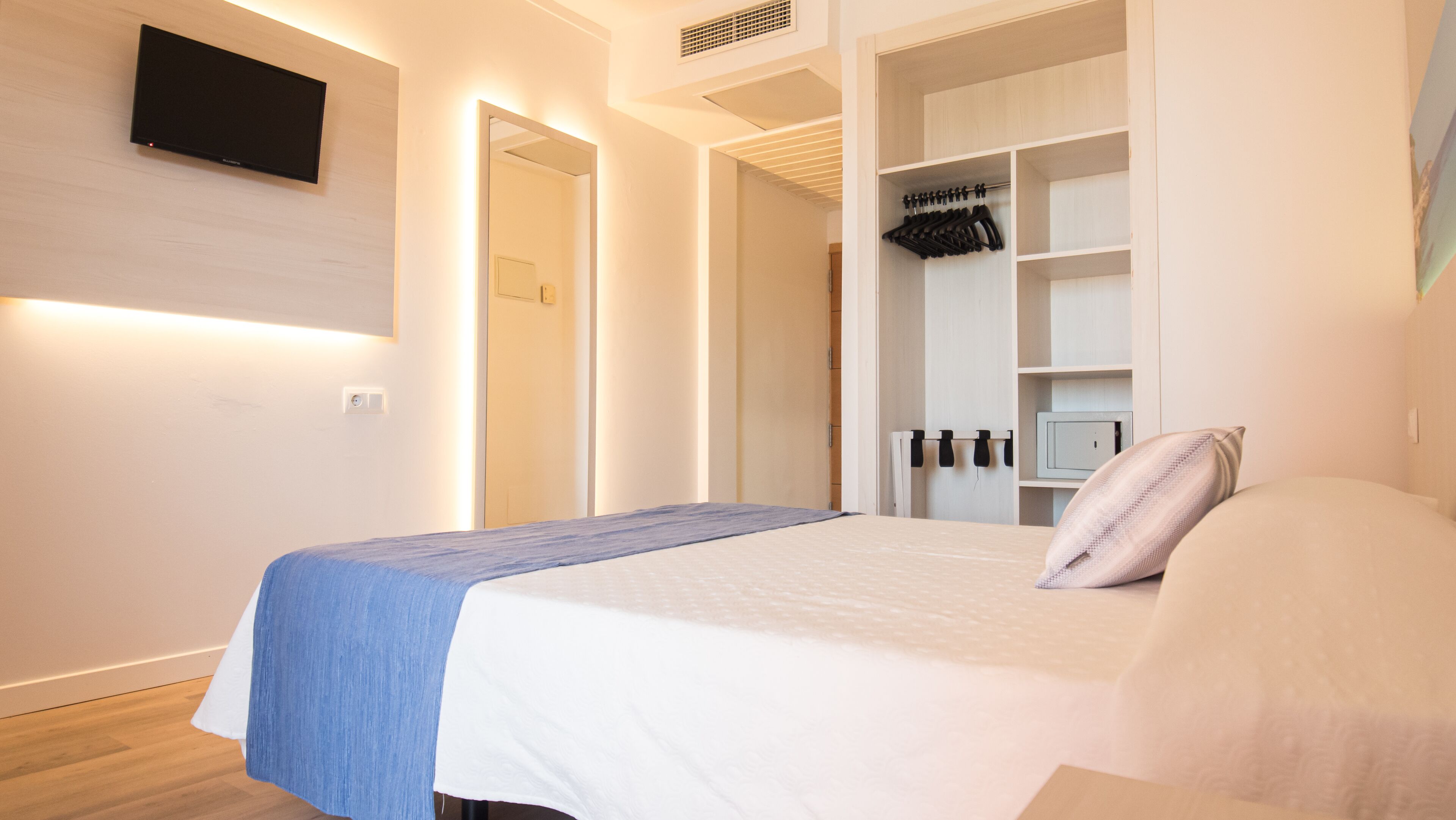 A bedroom with a bed, a wardrobe, a television mounted on the wall, and a mirror.