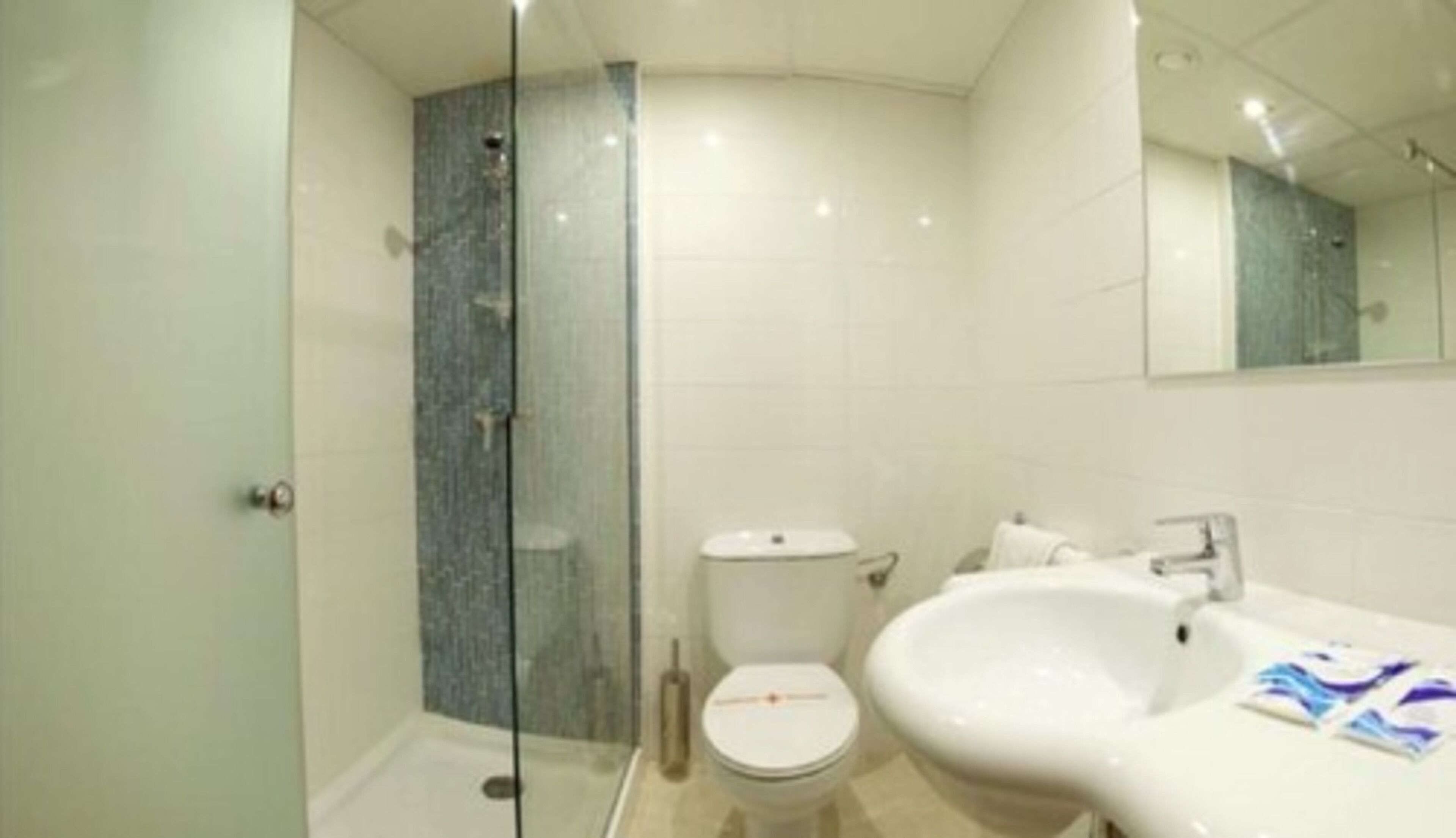 Une salle de bain moderne avec une douche à parois de verre, des toilettes blanches et un grand lavabo surmonté d’un miroir.