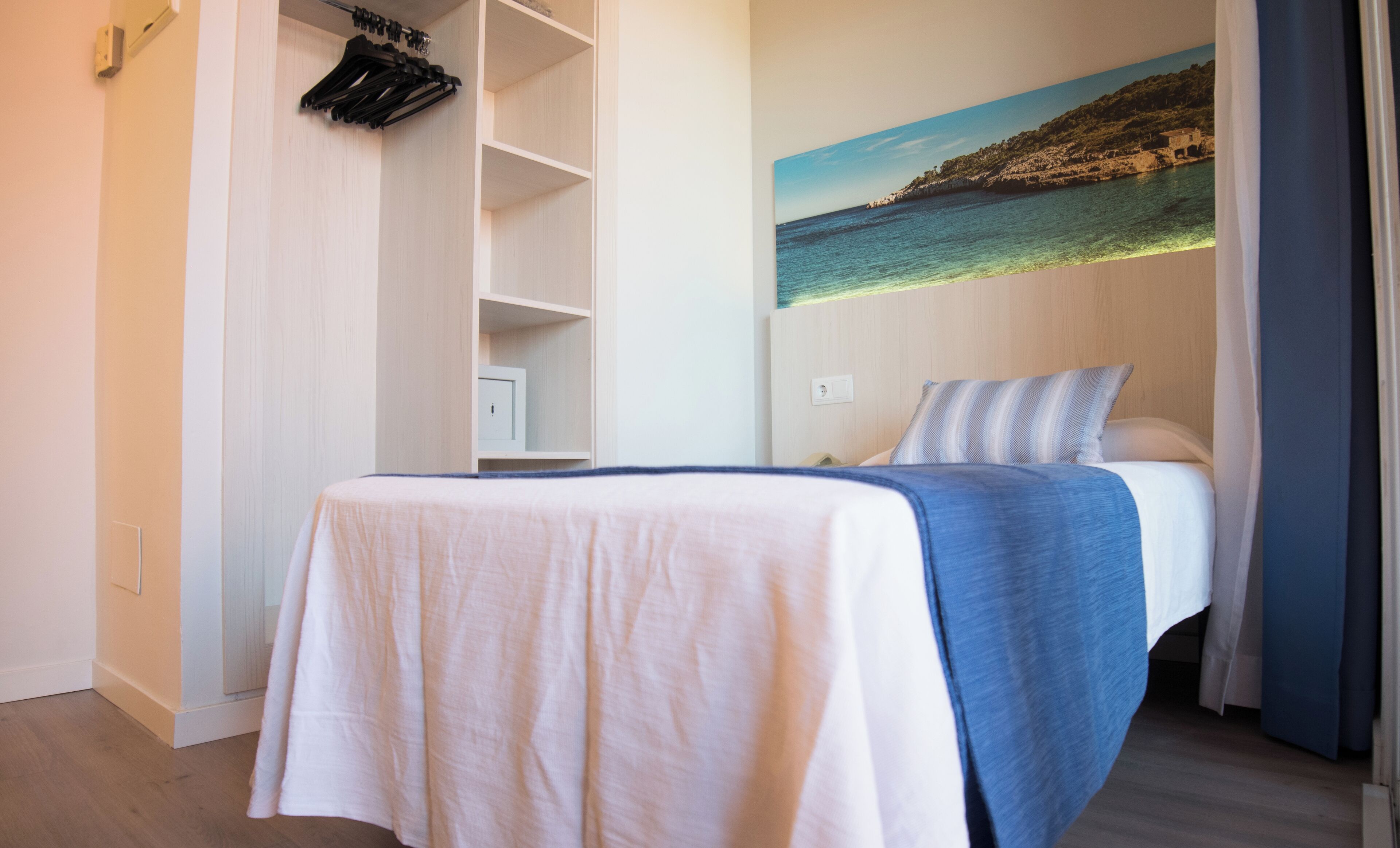 A bedroom with a bed, a wardrobe, and a painting of a coastal scene.