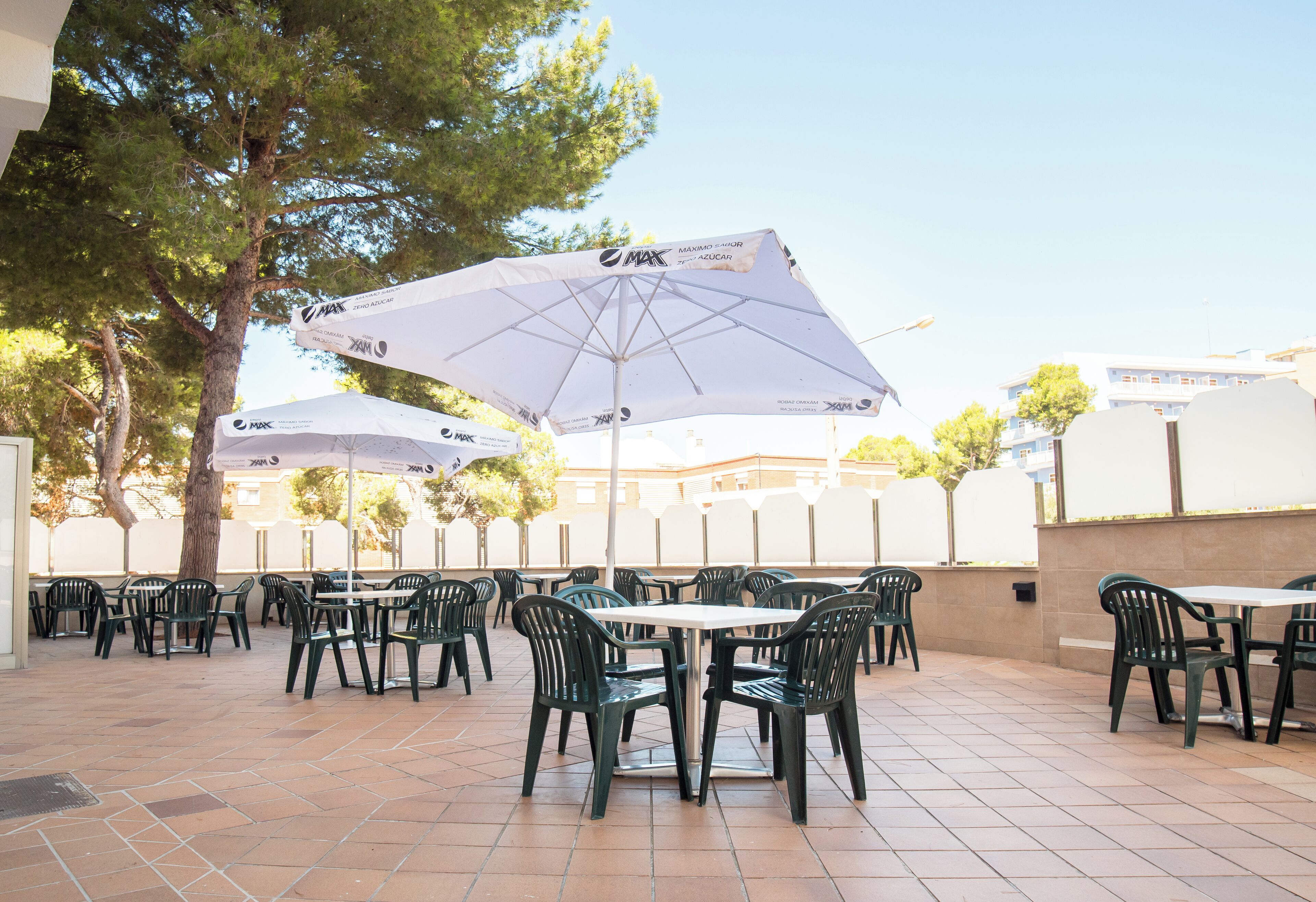 Eine Terrasse im Freien mit Tischen, Stühlen und Sonnenschirmen, sowie ein Baum.