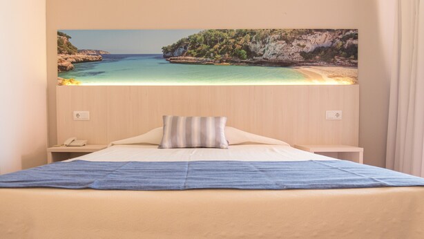 Une chambre à coucher avec un lit, une table de chevet, une lampe et un tableau représentant une scène de plage accroché au mur.