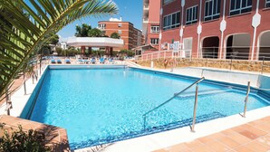 Une piscine à l’eau d’un bleu cristallin, entourée de chaises longues et d’un palmier.