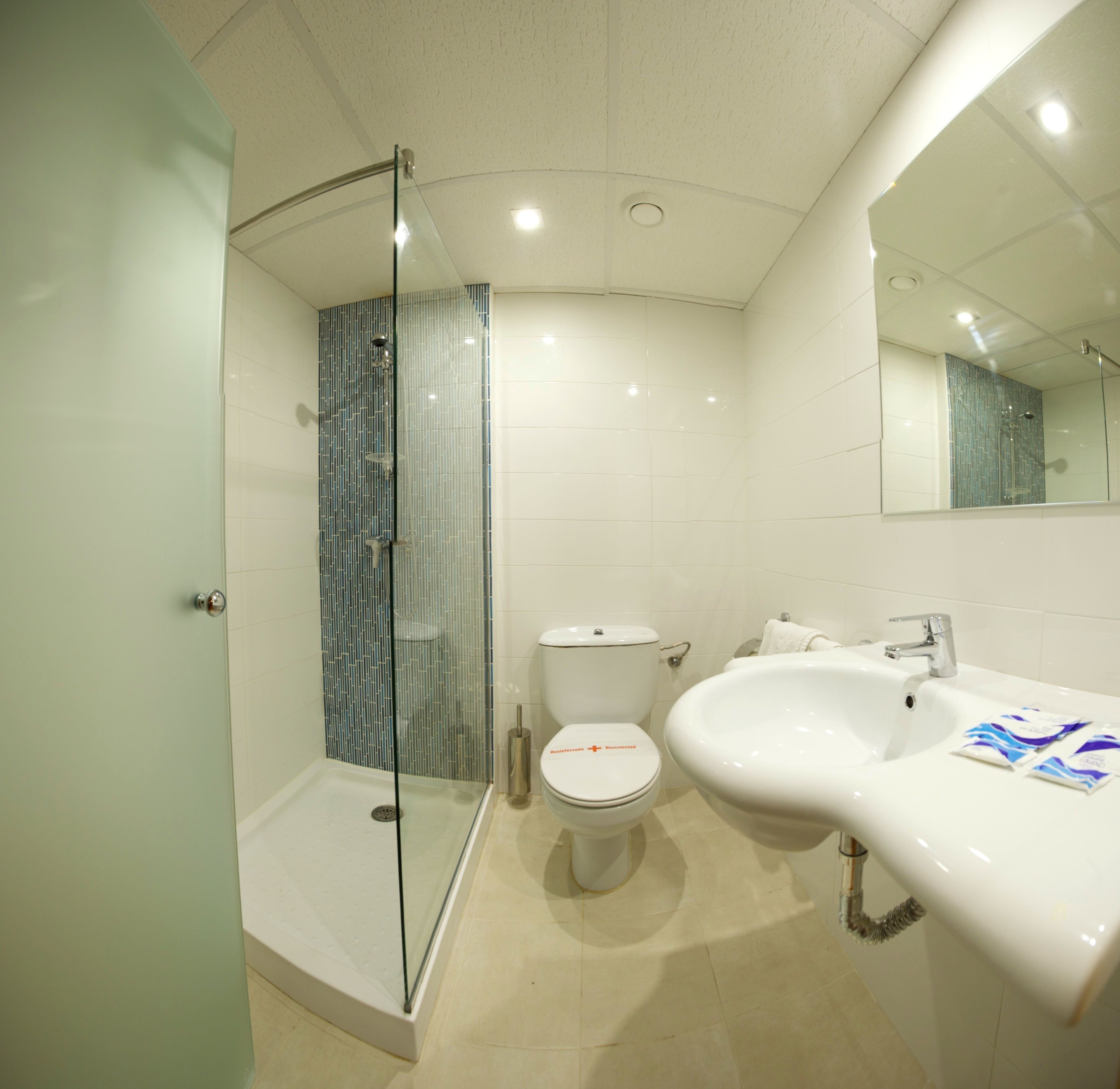Un baño moderno con ducha envuelta en cristal, inodoro blanco y un lavamanos grande con espejo arriba.