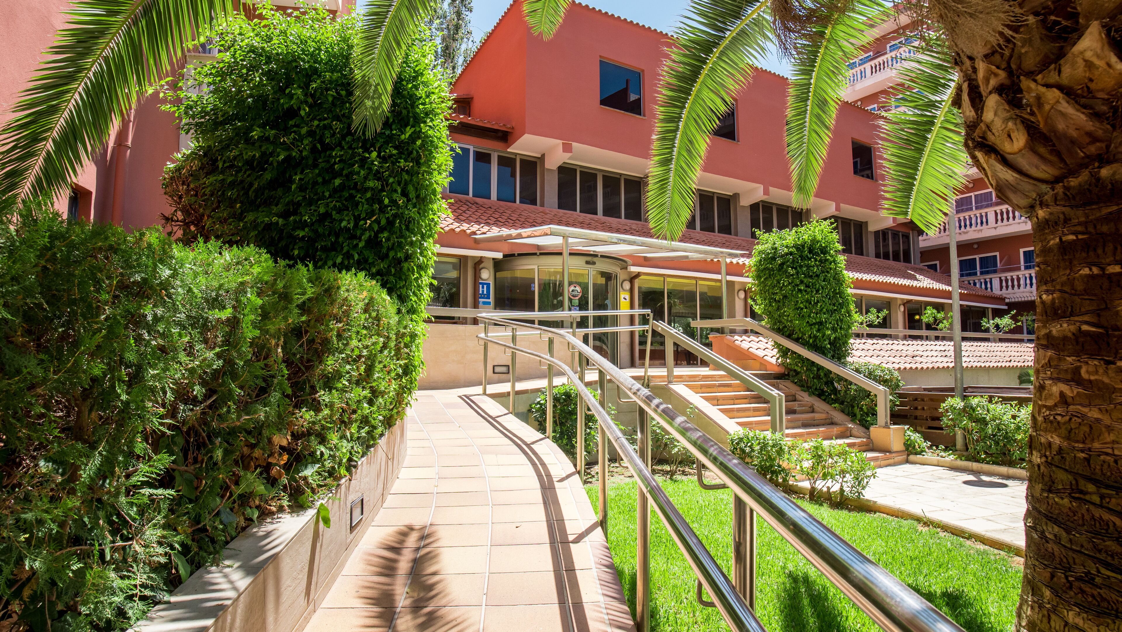 A hotel entrance with a glass door, a staircase, and a palm tree.