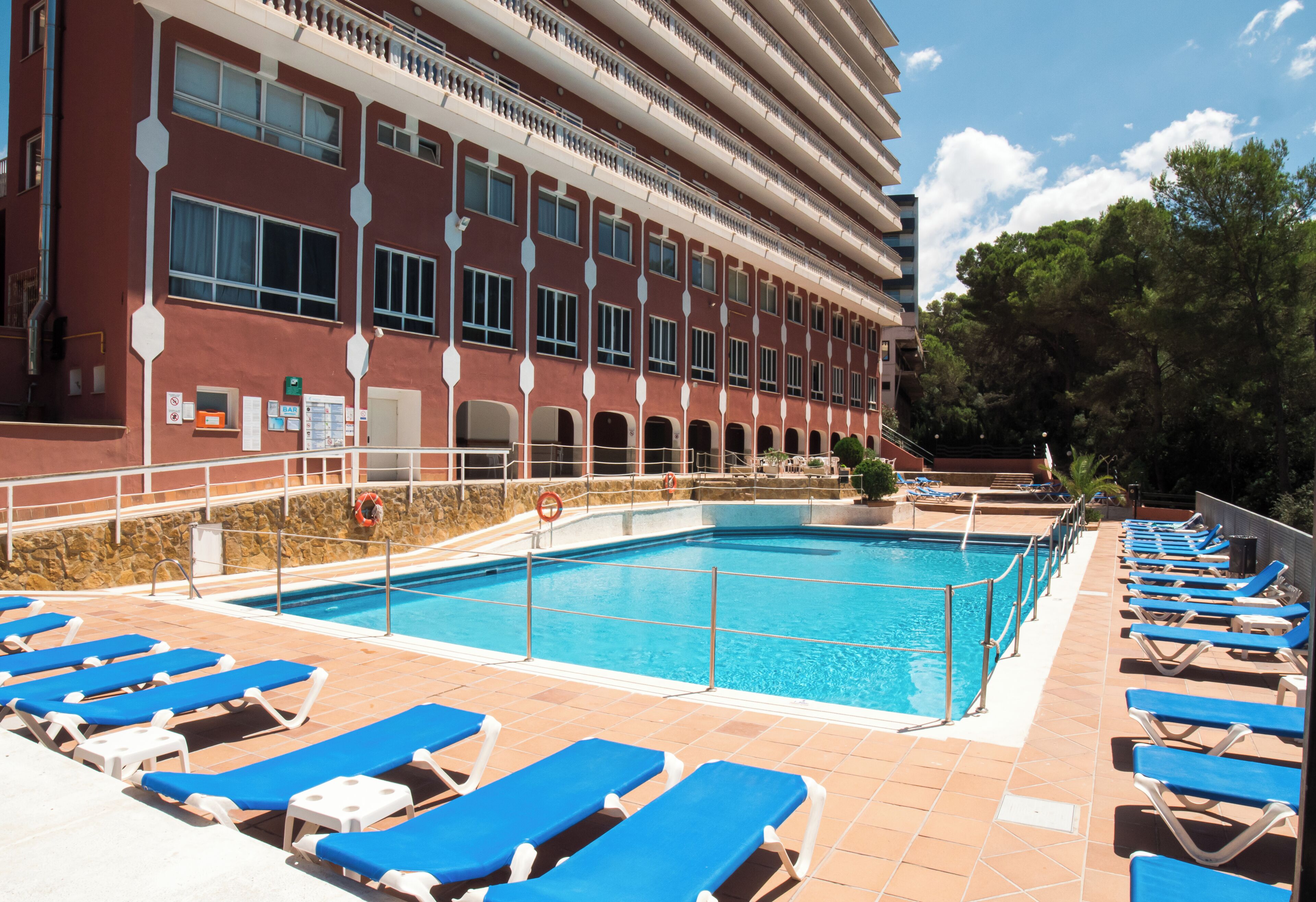 Un área de piscina con sillas reclinables azules y una piscina grande.