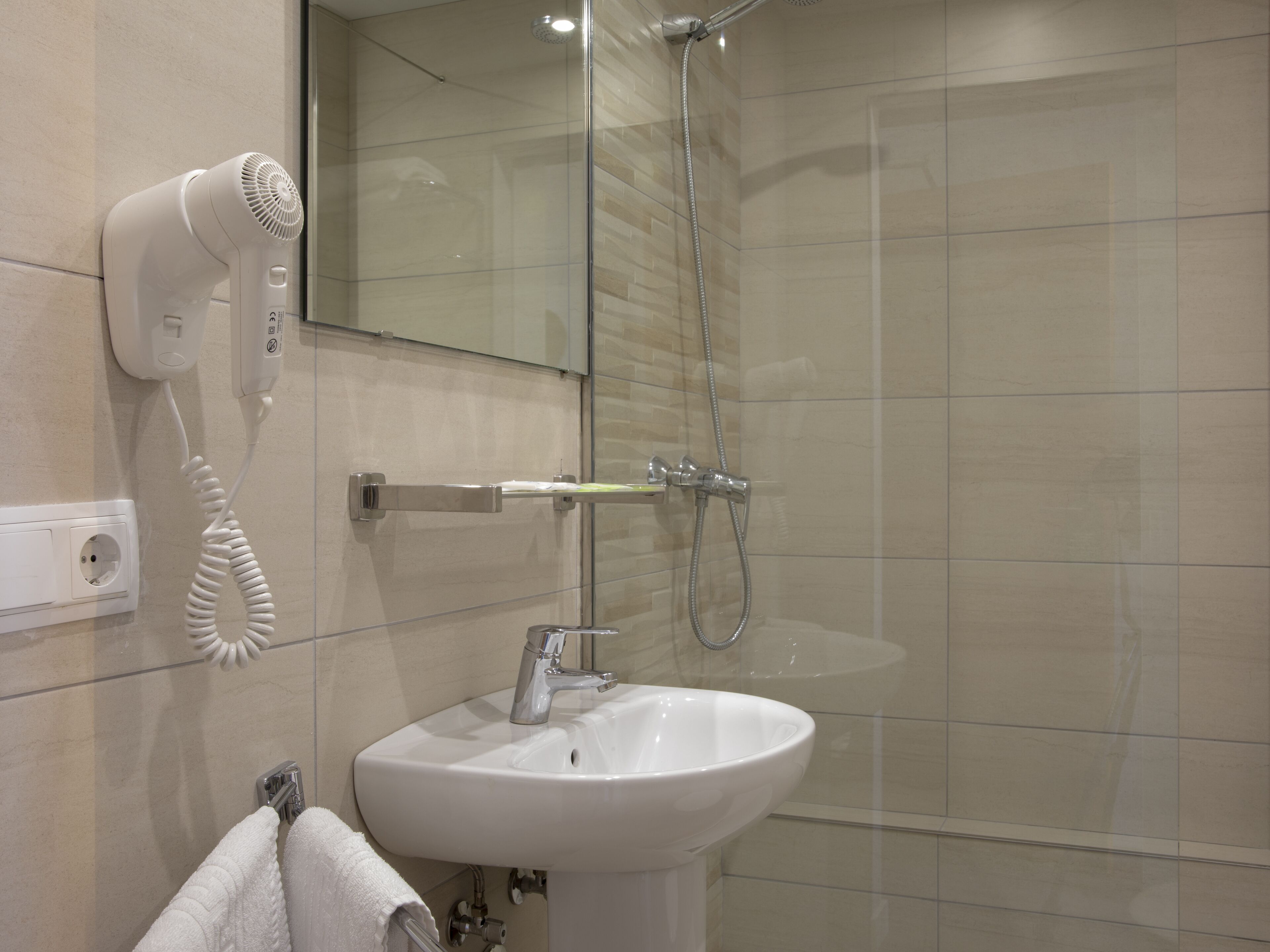 A modern bathroom with a glass shower enclosure, a white sink, and a hairdryer mounted on the wall.