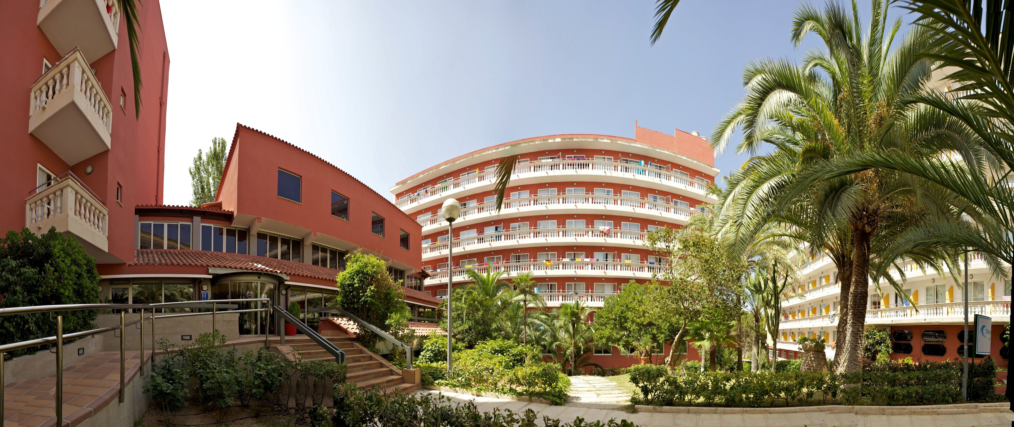 A multi-story hotel with a curved facade, outdoor stairs, and lush greenery.