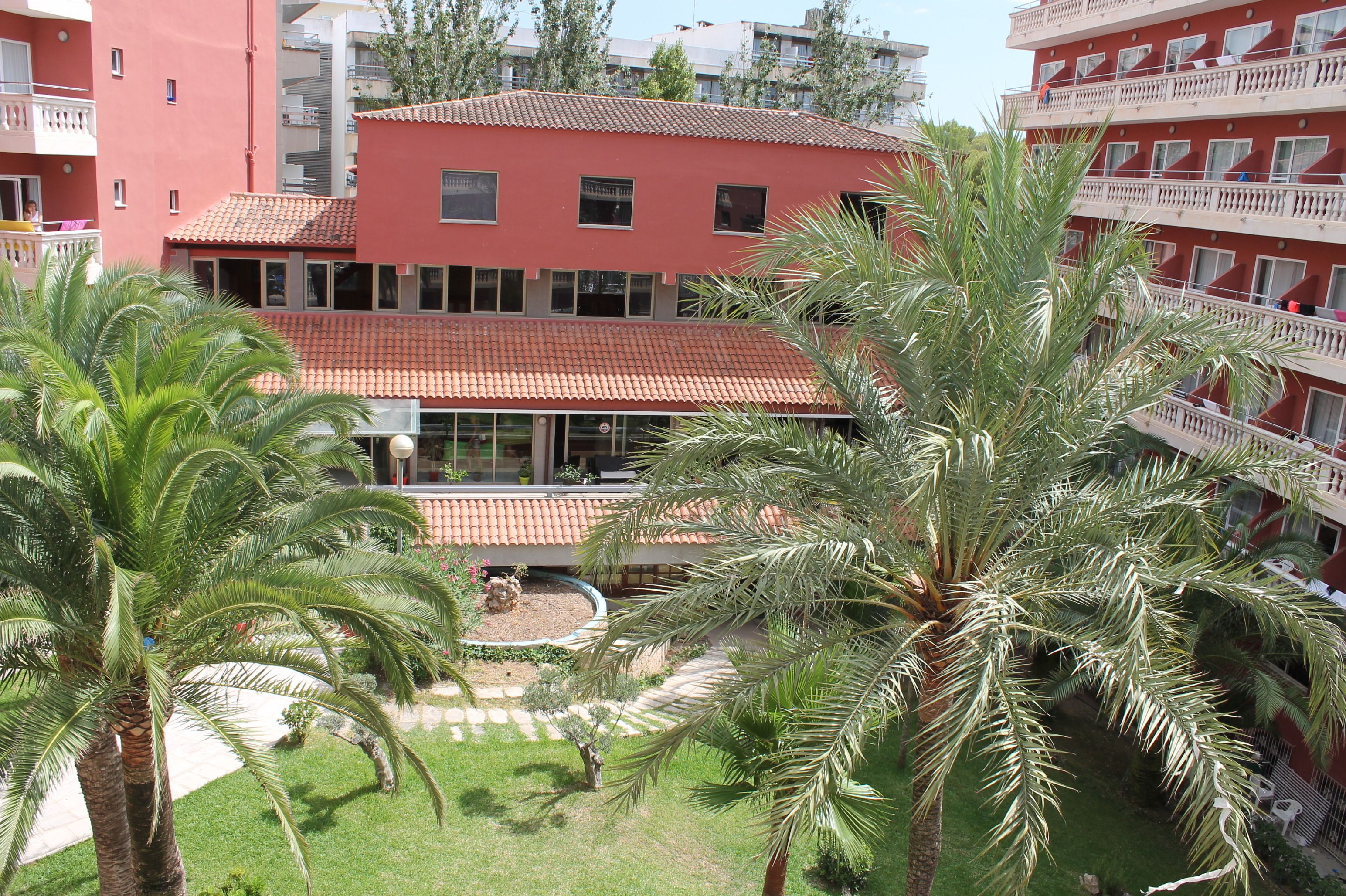 Un edificio de varios pisos con balcones, palmeras y techo de tejas rojas.