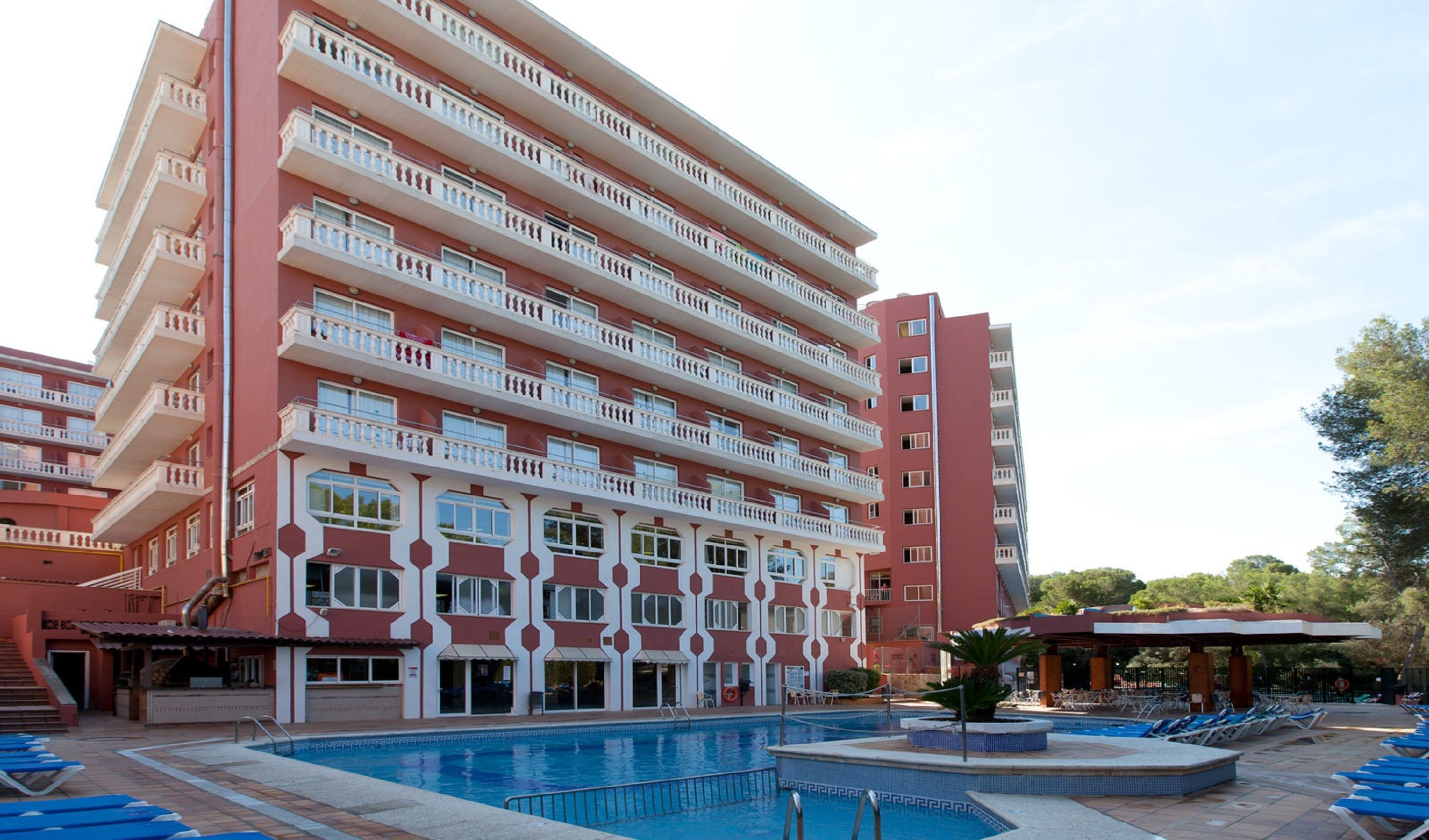 A multi-story hotel with a swimming pool and sun loungers.