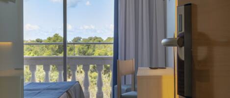 Une chambre d’hôtel avec un lit, une chaise, une petite table, un téléviseur fixé au mur et un balcon donnant sur un paysage verdoyant.