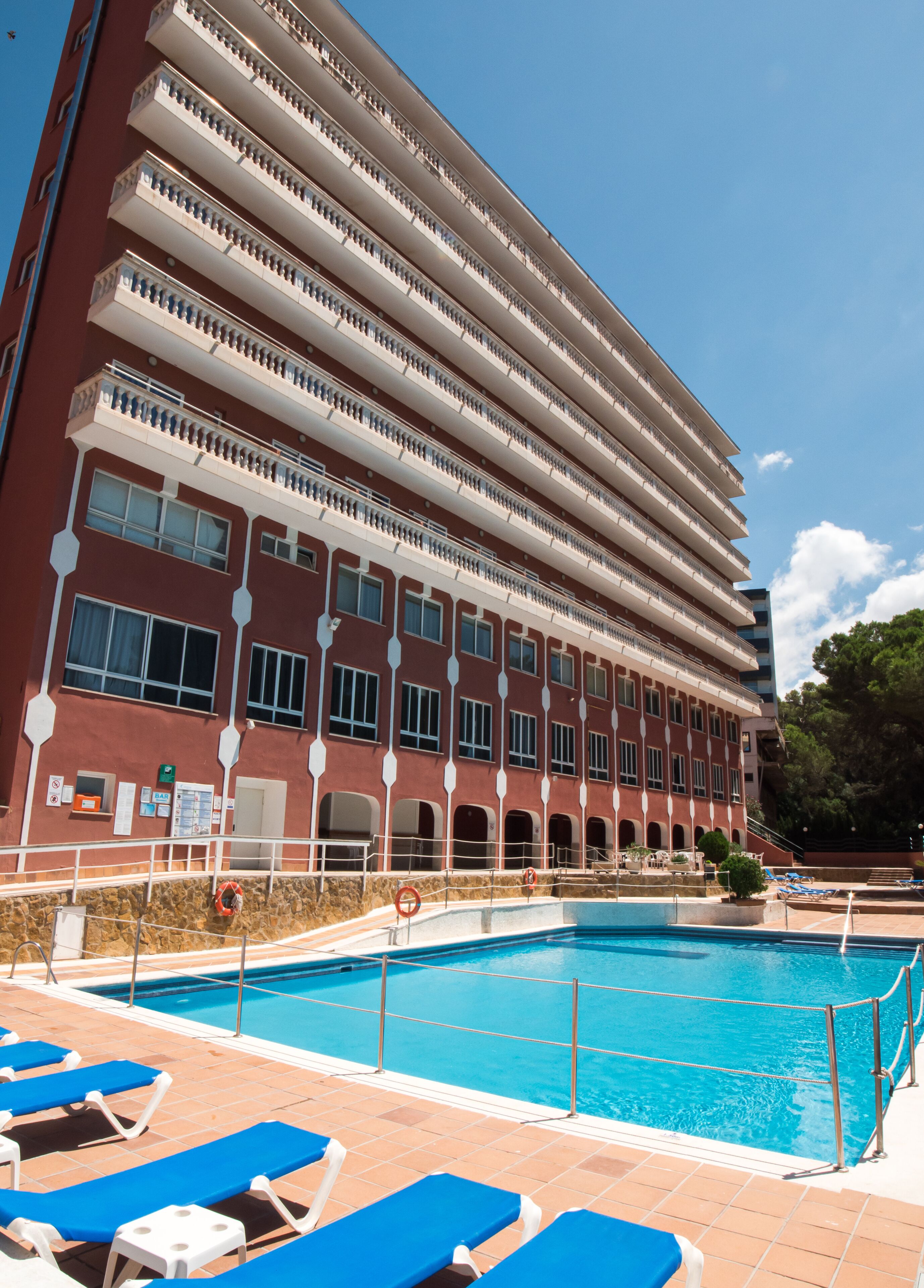 A multi-story hotel with a swimming pool and blue lounge chairs.