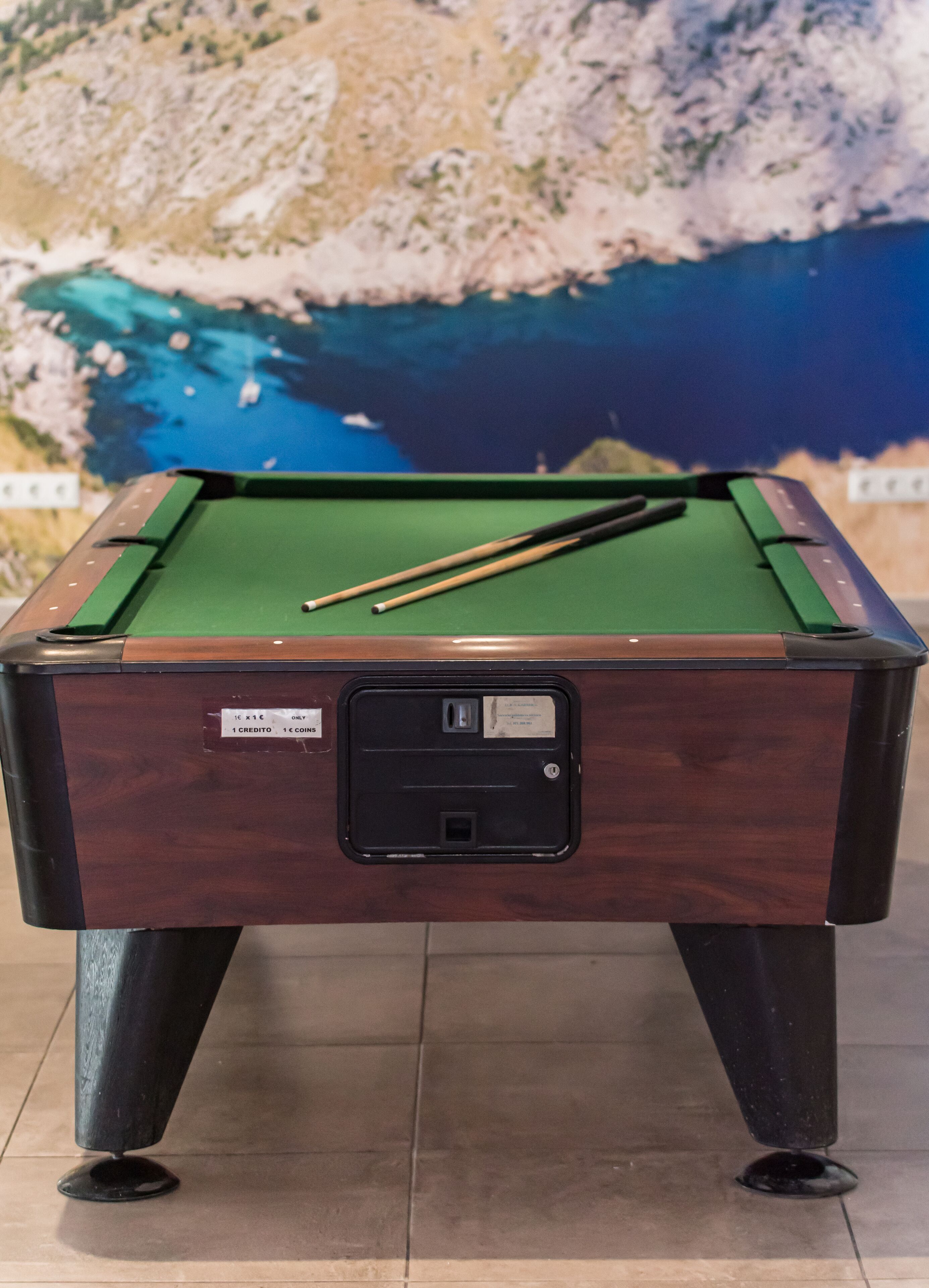 A pool table with a green felt surface, two pool cues, and a label indicating a 1 credit and 1 coin deposit.