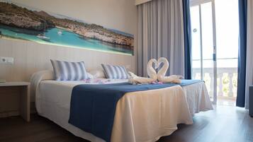 A hotel room with a large bed, a painting of a coastal scene, and a balcony with curtains.