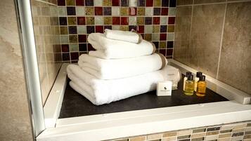 A bathroom with a tiled mosaic wall, a stack of white towels, and two bottles of bath products.