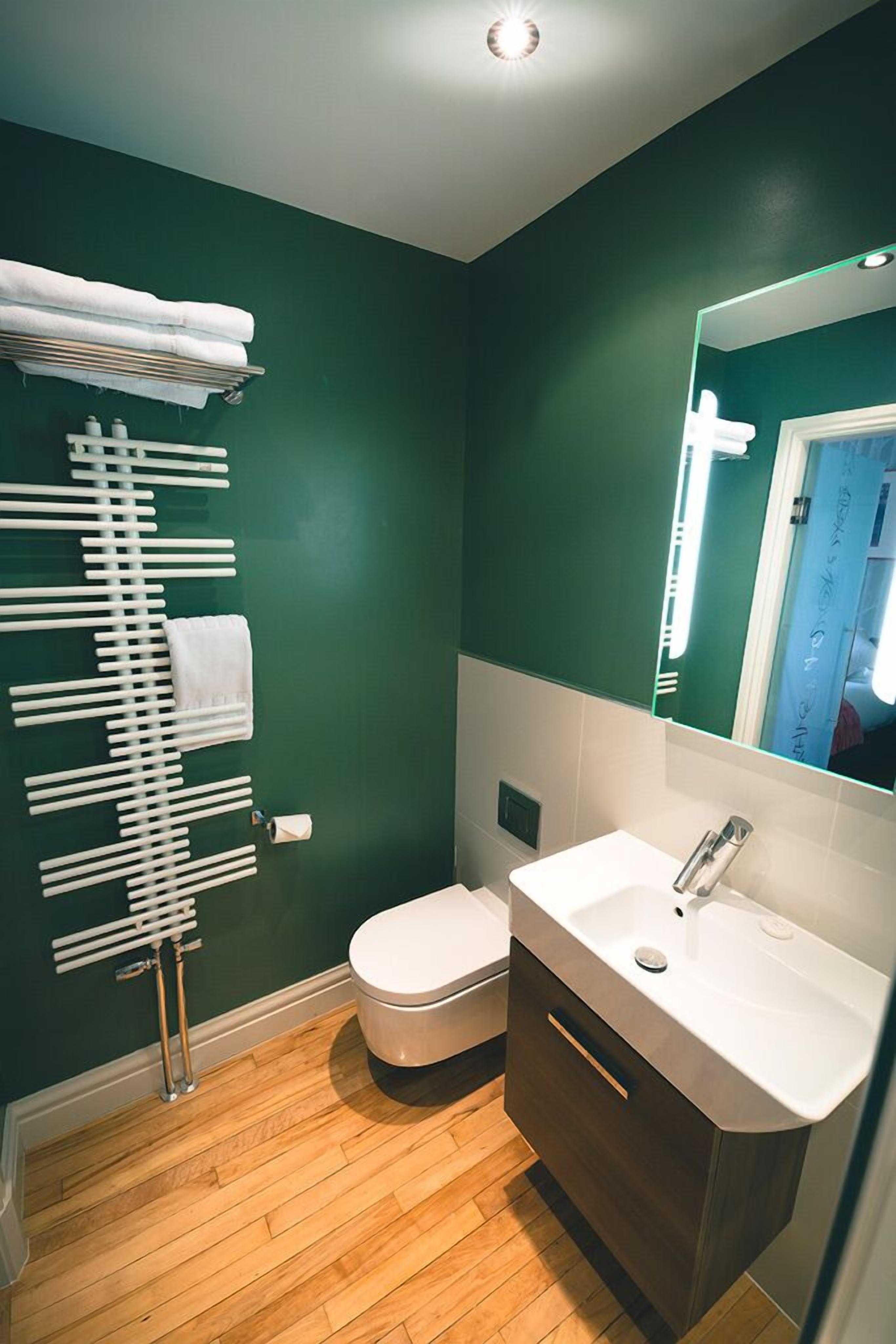 Een badkamer met een groene wand, een wit toilet, een witte wastafel met spiegel en een handdoekrek met handdoeken.