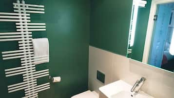 Een badkamer met een groene wand, een wit toilet, een witte wastafel met spiegel en een handdoekrek met handdoeken.