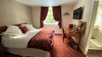 A hotel room with a bed, a desk, a chair, a mirror, and a window with curtains.