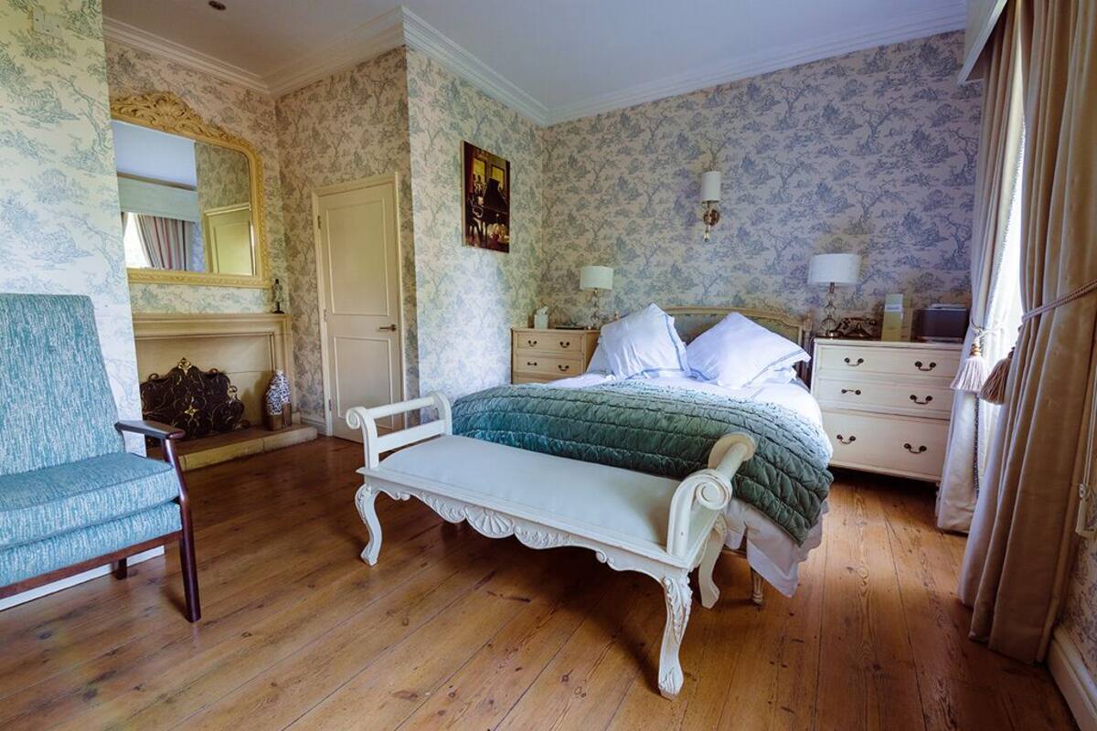 A bedroom with a bed, a bench, a dresser, a mirror, and a fireplace.