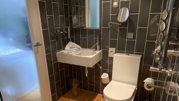 Een badkamer met houten vloer, een wit wastafelmeubel, toilet en douchehoek.