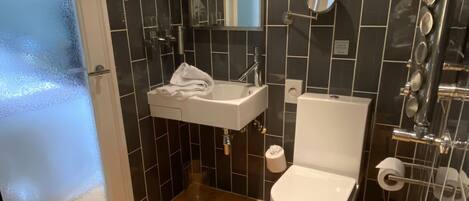 A bathroom with a wooden floor, a white sink, a toilet, and a shower area.