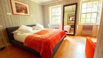 Een slaapkamer met een groot bed, een raam, een radiator en een spiegel.
